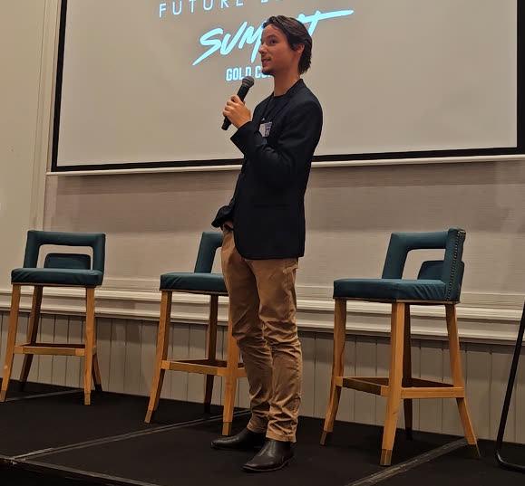 Dylan Amey speaking on stage with a microphone at the Future Leaders Summit